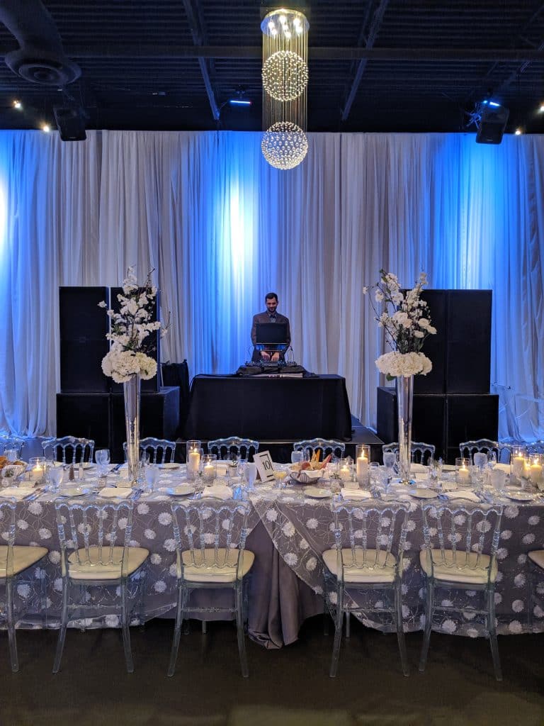 A DJ booth with uplighting and a draped backdrop at a Toronto wedding